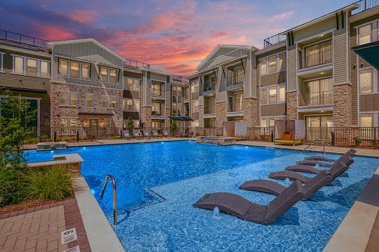 an apartment pool with two lounge chairs in front of an apartment building